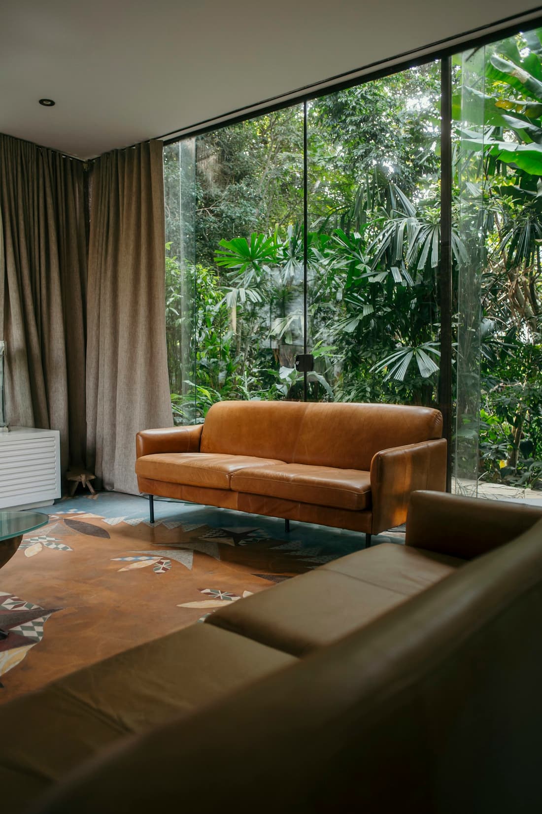 Sala de estar com poltronas de couro diante de uma janela ampla para a mata